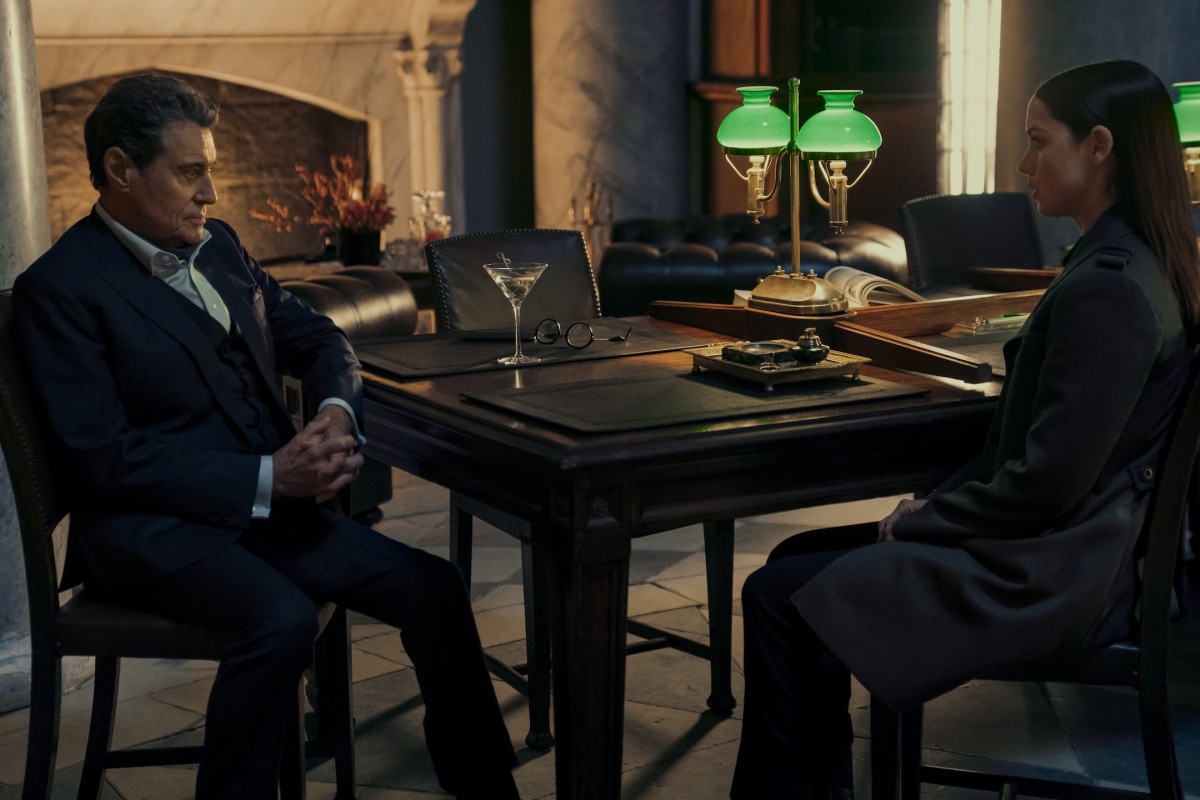 Ana de Armas ja Ian McShane istuvat pöydän ääressä elokuvassa Ballerina ( © Lionsgate)