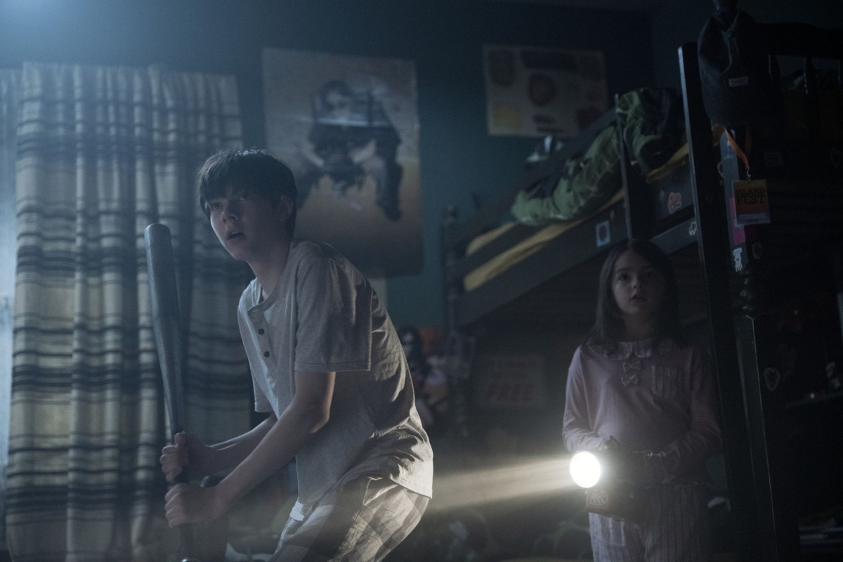 Lee Cronin's The Mummy -elokuvan näyttelijät seisovat pelokkaina pimeässä huoneessa (© Warner Bros. Pictures)