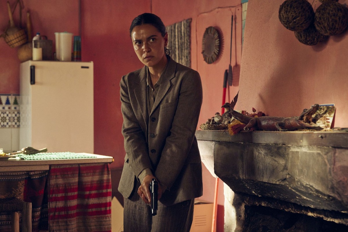 Lee Cronin's The Mummy -elokuvan näyttelijä seisoo ase kädessä huoneessa (© Warner Bros. Pictures)